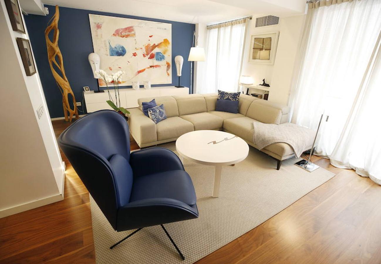 Las peticiones que Mariche Correcher planteó a la diseñadora creativa Carmen Bayarri estaban muy claras: que la casa tuviera muchos armarios, que la cocina y el salón estuviesen unidos pero a la vez se pudieran independizar y que la zona más tranquila de la casa albergara una suerte de suite en la que poder refugiarse después de la jornada de trabajo. Además le pidió que al entrar a la vivienda pudiera ver un ramo de flores. Con estas premisas, hace cuatro años se esbozó el proyecto en esta casa ubicada en una finca con carácter en pleno Ensanche valenciano. Para vestir el suelo escogieron madera de nogal, al igual que en las puertas que dividen las estancias. El resto de las puertas son blancas con las manivelas en negro y van de suelo a techo buscando potenciar la sensación de amplitud. En los baños instalaron porcelánico negro en el suelo que contrasta muy bien con el nogal. Carmen propuso ubicar junto a la entrada una escultura lacada flotante en rojo Ferrari que enmarca el espacio y permite ver el ramo de flores que reposa sobre la mesa del salón nada más entrar, que era uno de los deseos de la propietaria. La iluminación está integrada en la propia arquitectura. En lugar de obviar los pilares se decidió marcarlos de manera interna con filas de luz para ofrecer un ambiente casi escultórico. 