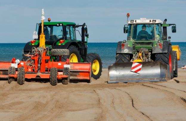 Dos tractores llevan arena de la zona del paseo marítimo a la orilla del mar. 