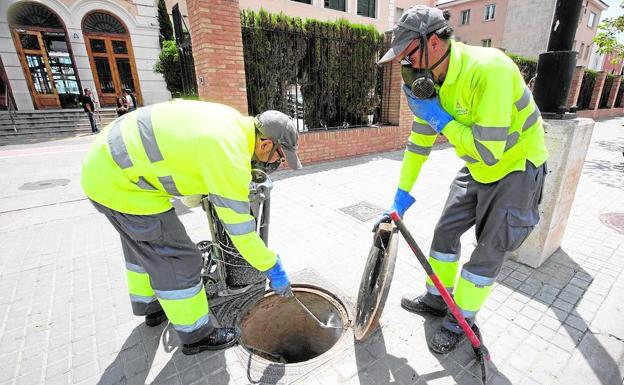 Pintura. Dos operarios aplican un producto para frenar la proliferación de cucarachas en el alcantarillado.