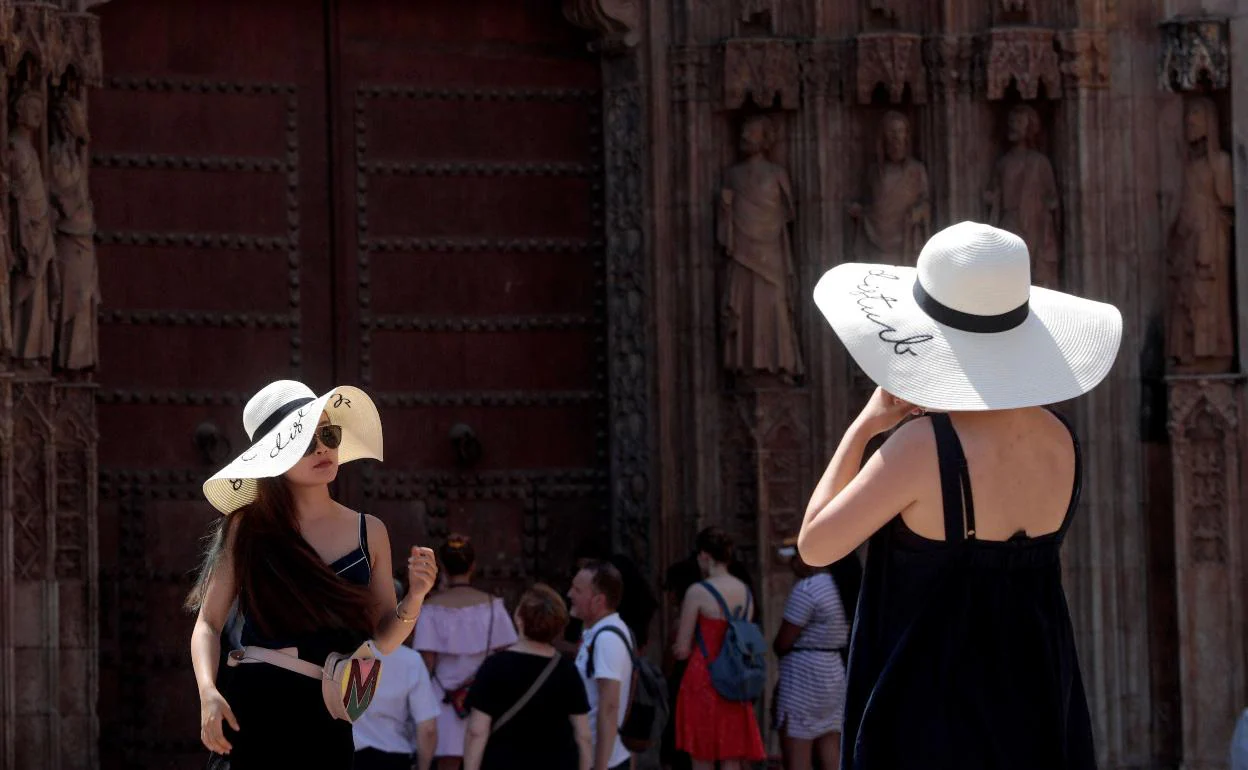 Dos turistas recorren el casco antiguo de la ciudad protegidas con sombreros.