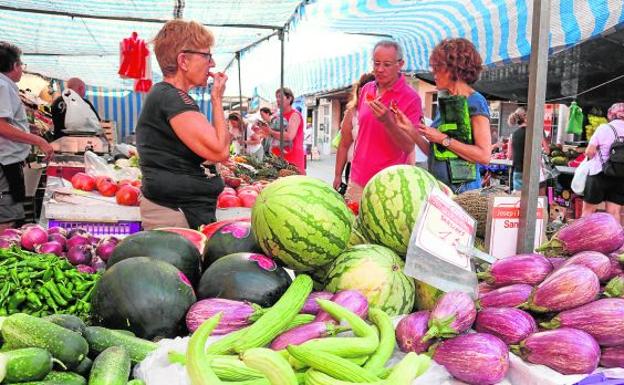 Varios vecinos degustan fruta en uno de los puestos del mercadillo de que se celebra los viernes en Dénia. 