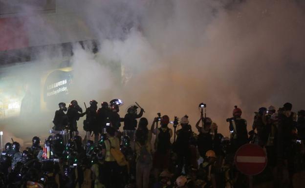 Los gases lacrimógenos envuelven a los manifestantes y los medios de comunicación que siguen los disturbios en Hong Kong, mientras que las fuerzas de seguridad esperan para cargar.