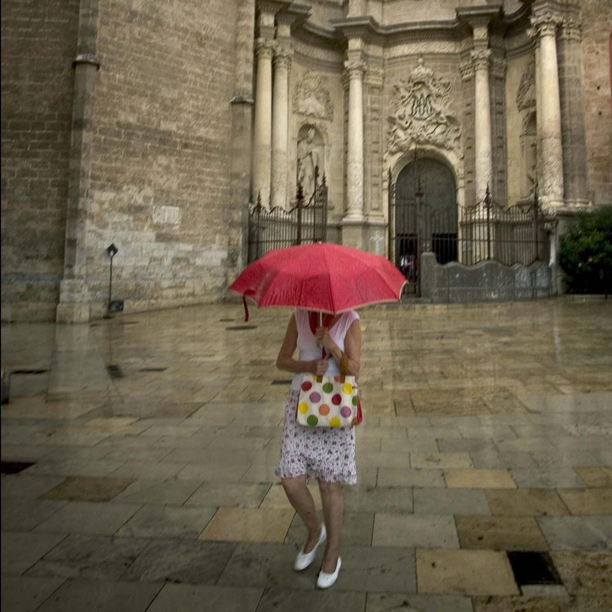 Una mujer, con un paraguas, ante la puerta de la Catedral de Valencia.