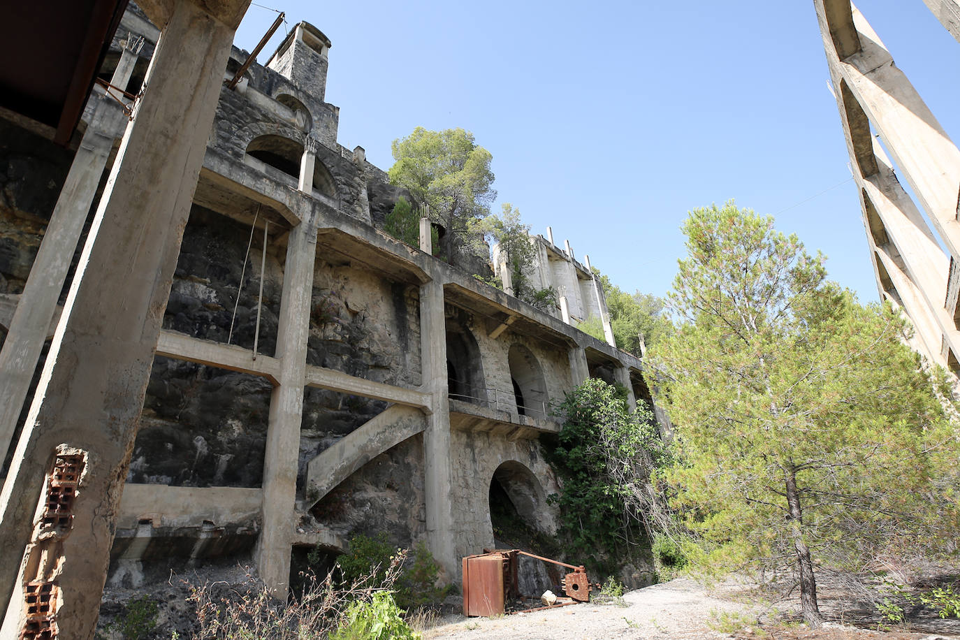 La cementera de Benagéber (Valencia) | La enorme construcción todavía se contempla desde lo lejos, como un colosal castillo de hormigón entre agua y maleza. Construida en la década de los cuarenta, fue gestionada por la misma empresa que se encargó del embalse, Portolés y Cía, que se convertiría en una de las principales compañías de obras públicas tras la Guerra Civil. La construcción del pantano de Contreras también corrió a cargo de esta firma, prueba de su estrecha colaboración laboral con el gobierno franquista. En aquella época, la mayoría de los habitantes de Benagéber eran los trabajadores de las obras del embalse y la cementera. Por ello, cuando en 1955 finalizaron los trabajos para la formación del pantano, la mayoría de la población emigró y el lugar quedó sumido en la escalofriante quietud que, a día de hoy, le sigue caracterizando. 
