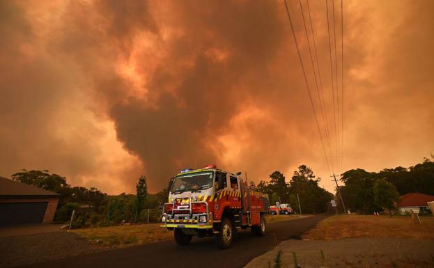 Un camión de bomberos aparcado en una carretera de Bargo, al suroeste de Sídney, mientras un incendio tiene lugar a sus espaldas.