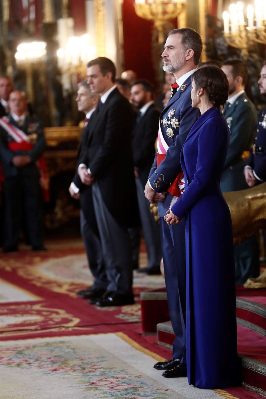 Felipe VI, acompañado por la Reina Letizia, ha presidido este lunes la ceremonia de la Pascua Militar en el Palacio Real. Para la ocasión, Doña Letizia ha elegido un elegante vestido de estilo esmoquin en azul intenso. La Reina ha combinado el diseño, largo hasta los pies, con unos zapatos stilettos en color negro y un peinado recogido acabado en un moño bajo.