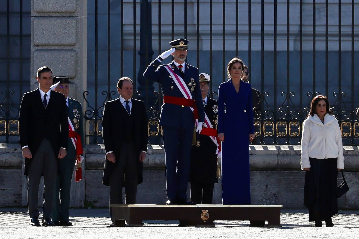 Felipe VI, acompañado por la Reina Letizia, ha presidido este lunes la ceremonia de la Pascua Militar en el Palacio Real. Para la ocasión, Doña Letizia ha elegido un elegante vestido de estilo esmoquin en azul intenso. La Reina ha combinado el diseño, largo hasta los pies, con unos zapatos stilettos en color negro y un peinado recogido acabado en un moño bajo.