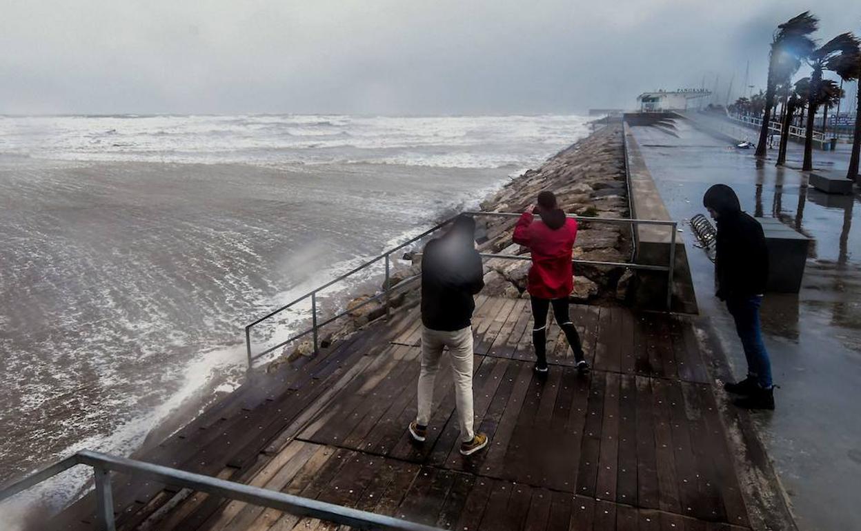 Tres jóvenes fotografían el temporal en el Paseo Marítimo de Valencia.