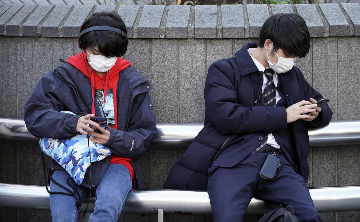 Dos jóvenes con mascarillas en un banco en el distrito de Shibuya, Tokio.