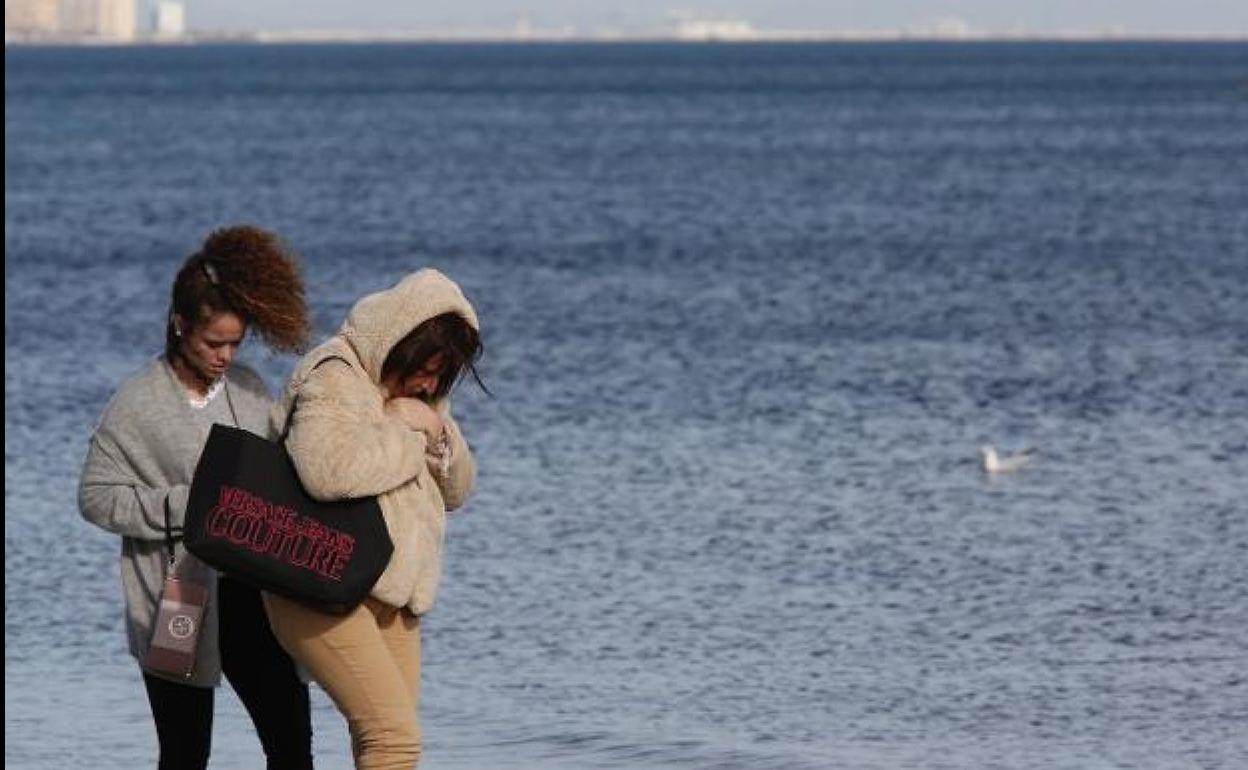 Dos mujeres se protegen del viento en la playa de la Malvarrosa. 