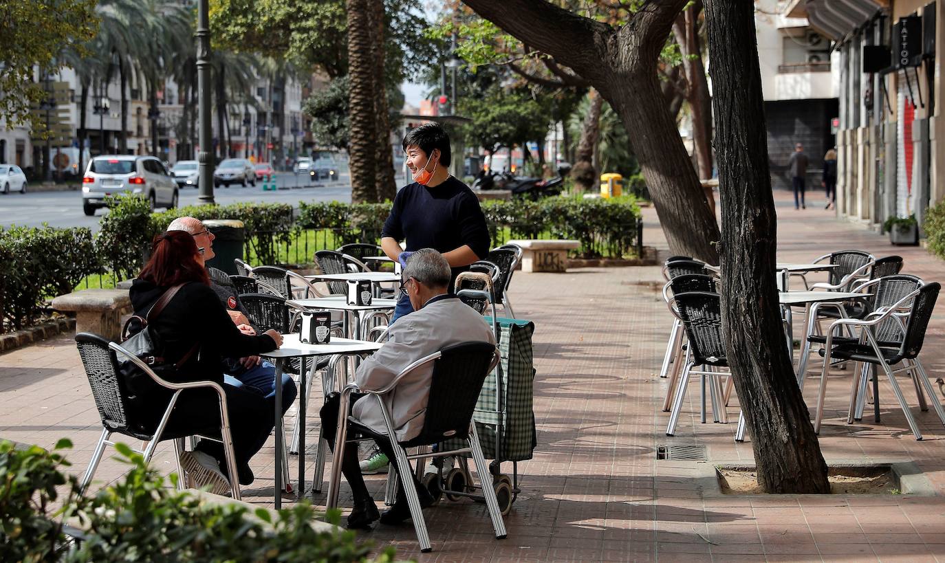 Un camarero, protegido con guantes y mascarilla, atiende a unos clientes en una terraza de Valencia.