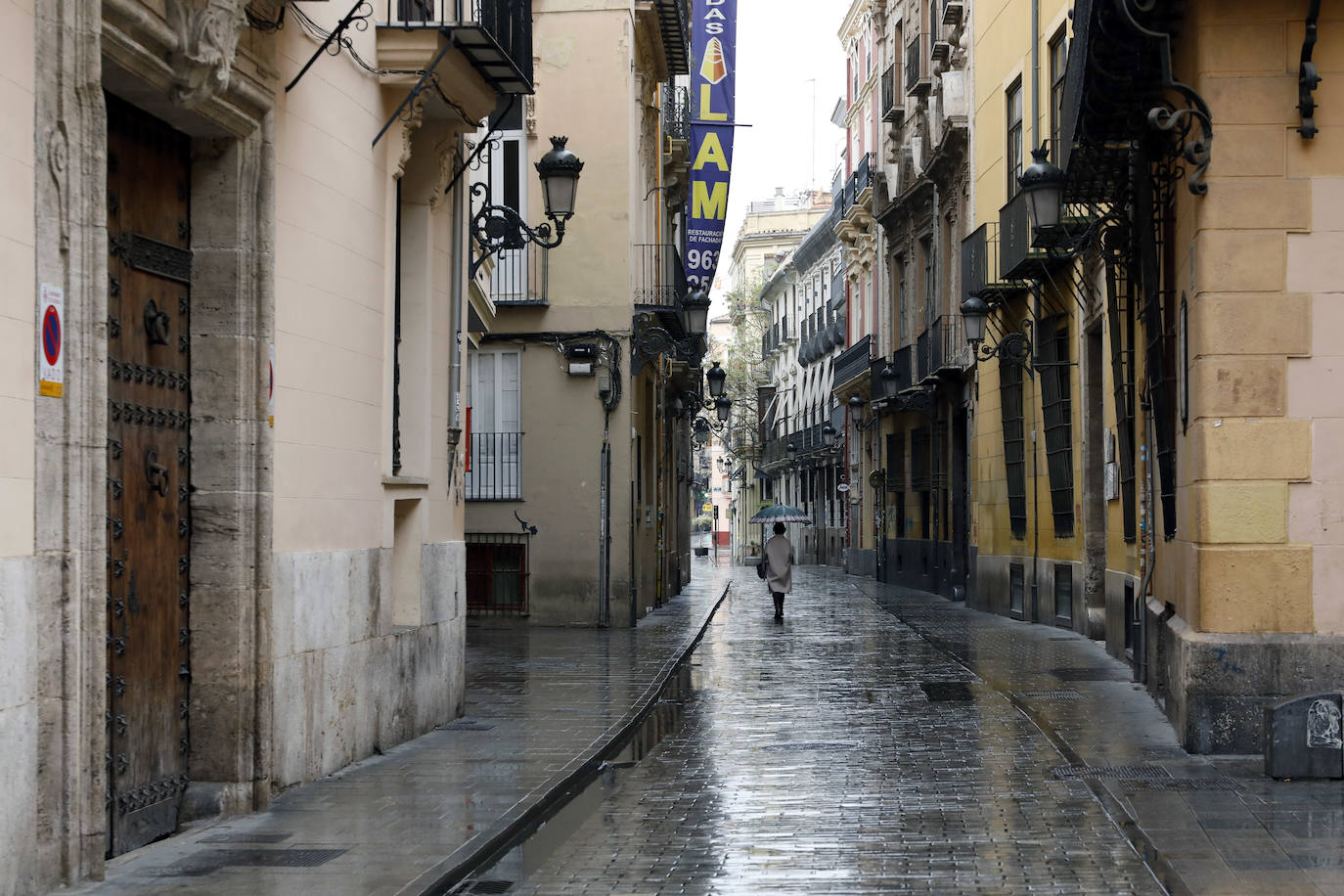 Lunes 16 de marzo. Una mujer camina bajo su paraguas por una de las calles del casco antiguo de Valencia, sin nadie más en la vía.