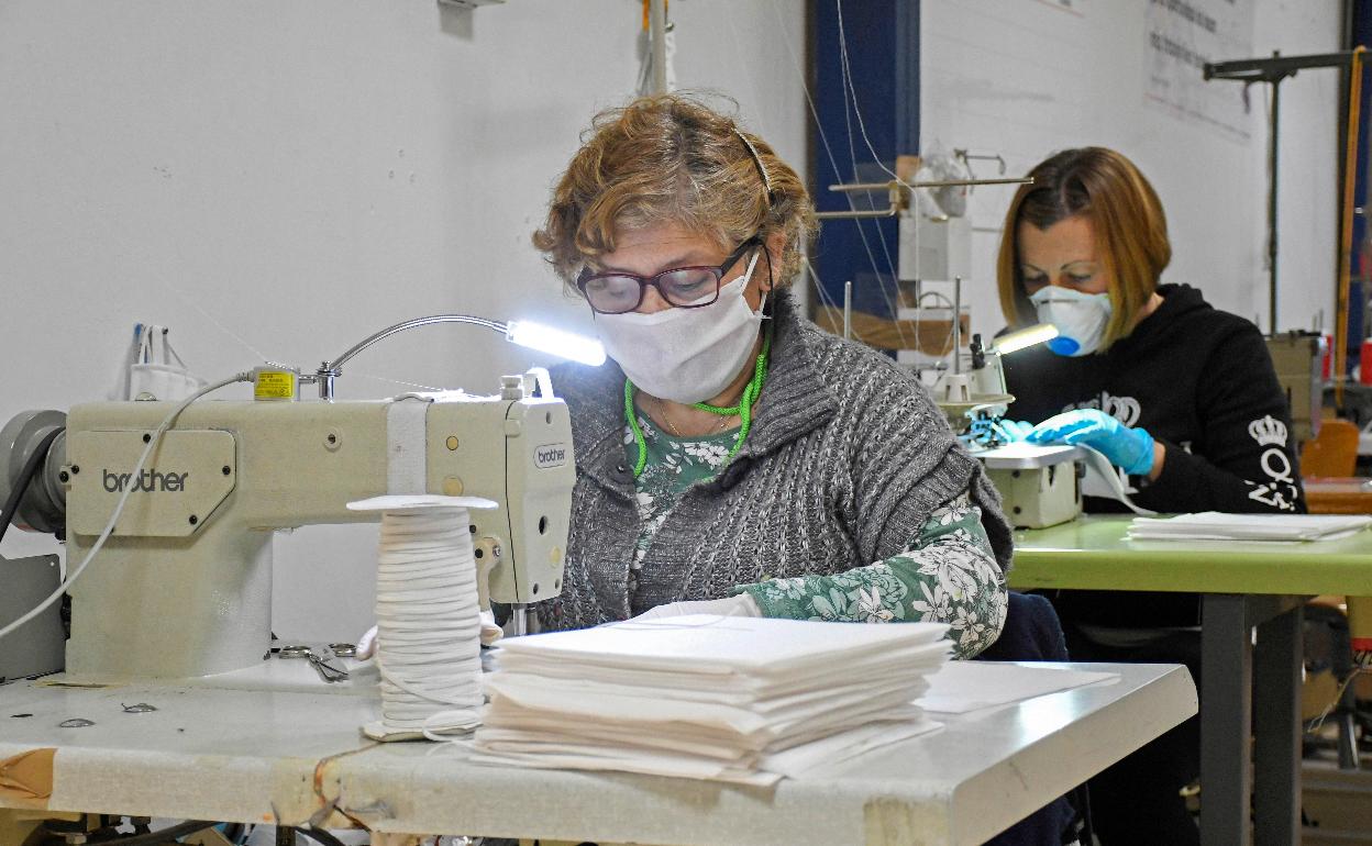 Dos mujeres cosen mascarillas en un talles. 