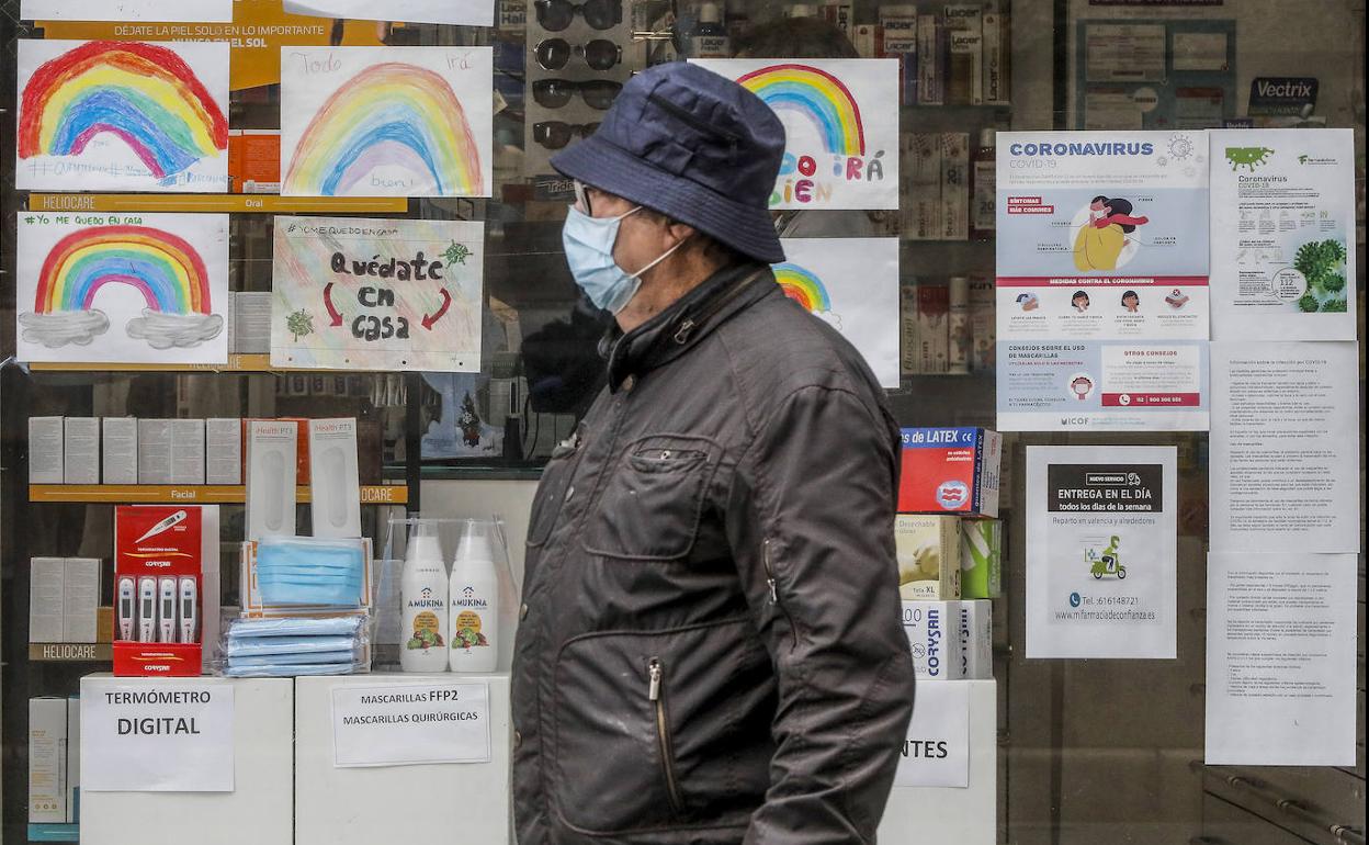 Un hombre con mascarilla pasa junto a una farmacia.