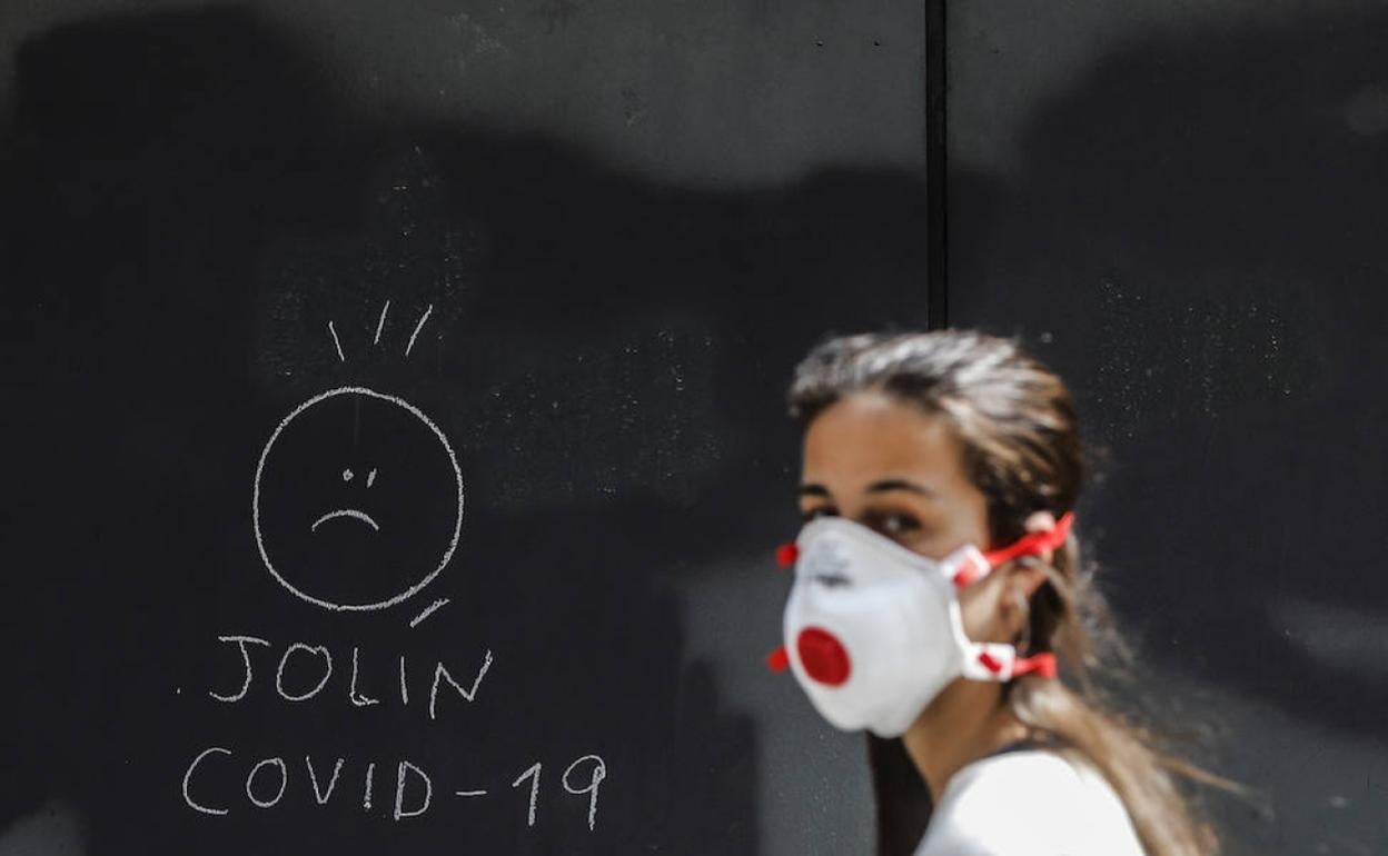 Una joven con mascarilla pasa por delante de una pintada sobre el coronavirus. 