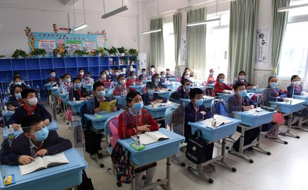 Estudiantes con mascarillas se sientan en una clase con mamparas en sus escritorios en una escuela de Chongqing, China. 