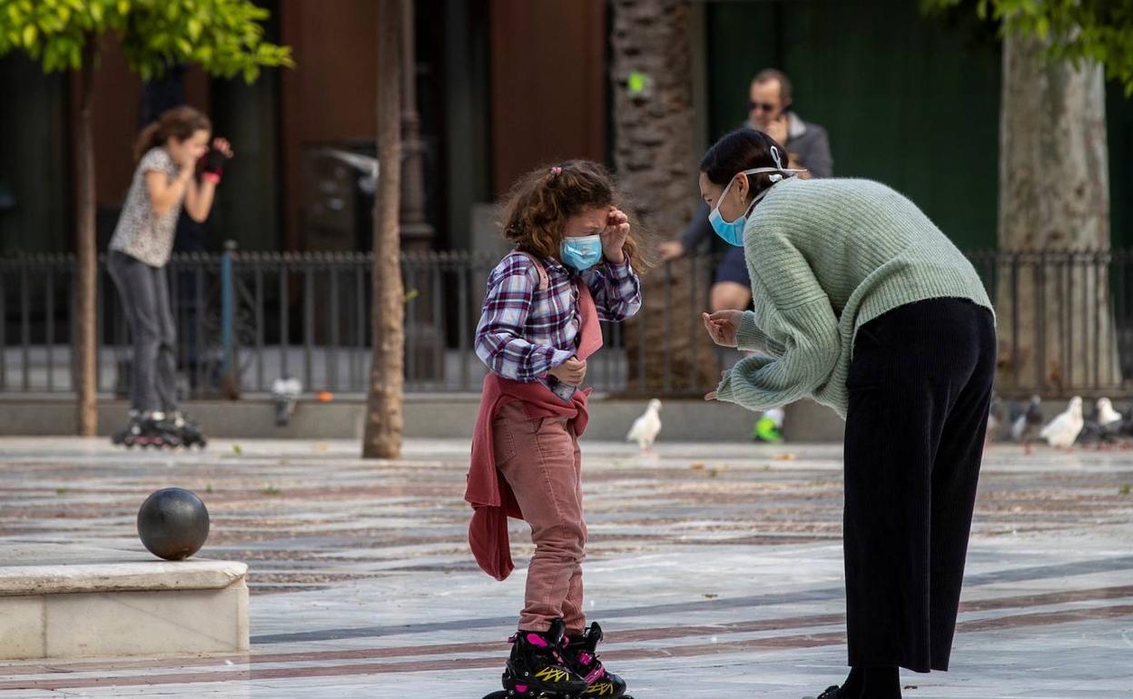 Una niña en patines y con mascarilla conversa con su madre en Sevilla. 