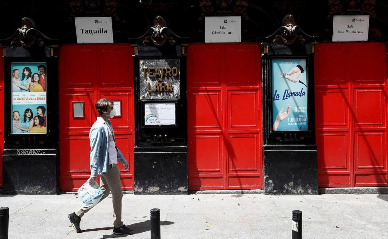 Un hombre ataviado con una mascarilla sanitaria pasa frente al Teatro Lara de Madrid.