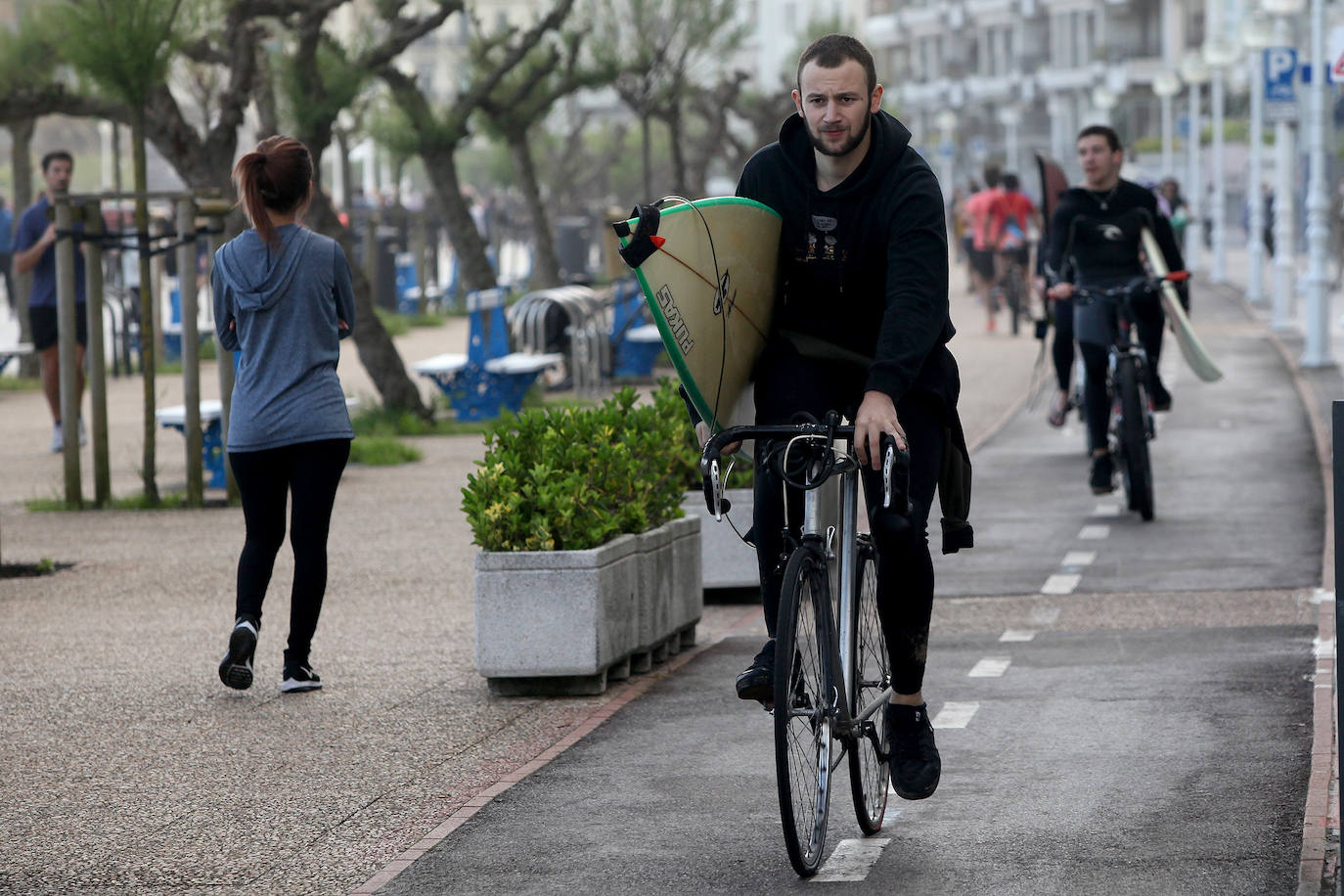 Dos jóvenes van con su bicicleta y su tabla de surf en San Sebastián. 