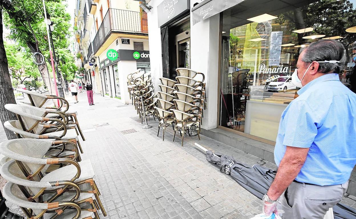 Hostelería. Un hombre pasa por delante de un bar con sillas preparadas en la terraza.