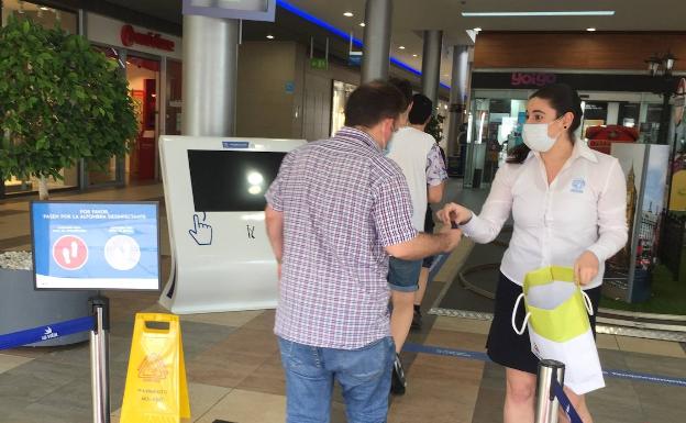 Una empleada de La Vital en Gandia entrega una mascarilla a un cliente.