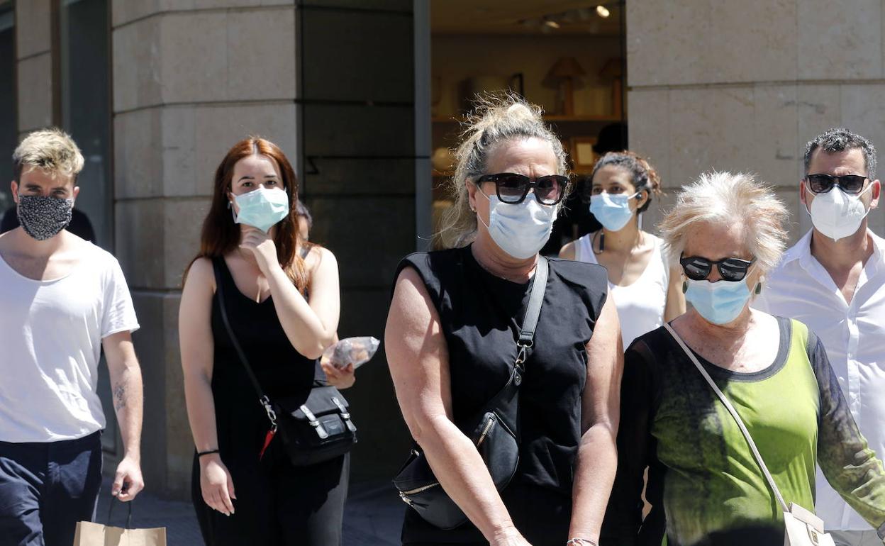 Varias personas paseando por el centro de Valencia con mascarillas. 