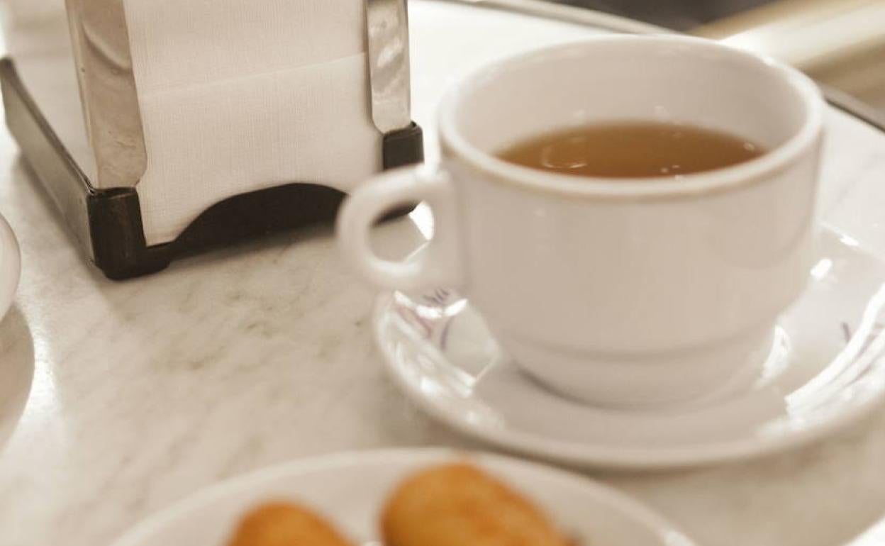 Una mesa de un bar con una tapa, un café y un servilletero. 