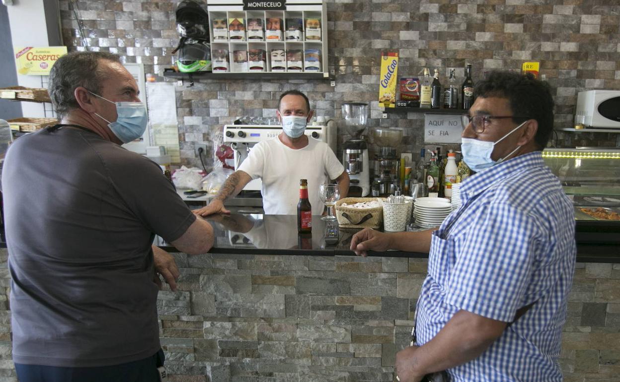 Un camarero atiende a dos clientes con mascarilla tomando un refresco en la barra de un bar. 