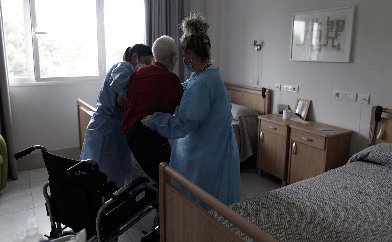 Trabajadoras de un centro de mayores ayudan a un anciano a sentarse en una silla de ruedas. 