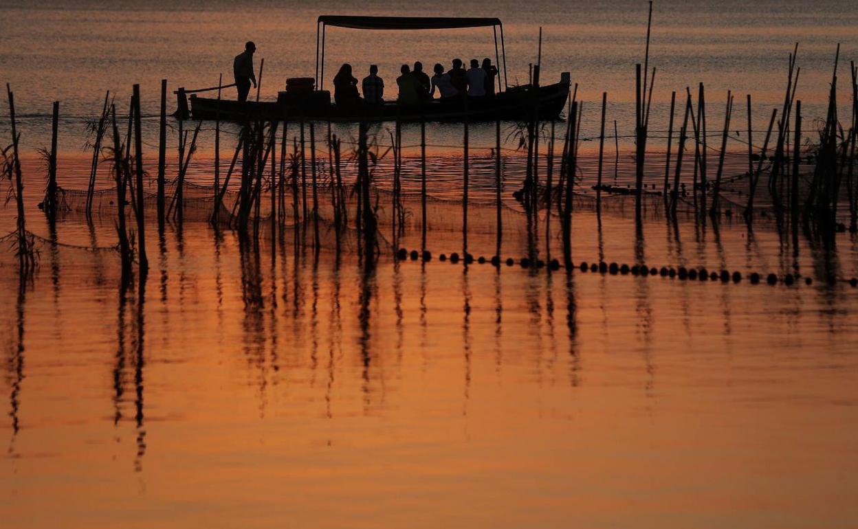 Una barca con turistas navega junto a un puesto fijo de pesca en la Albufera. 