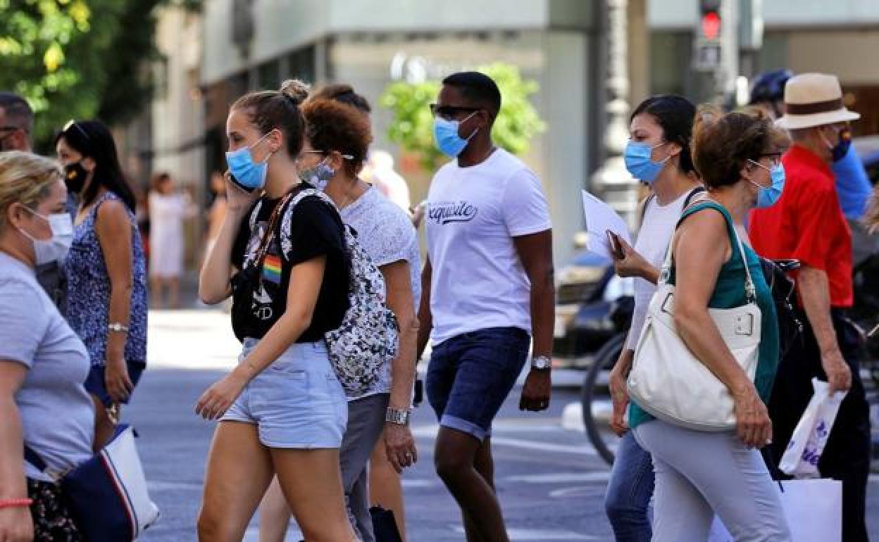 Varias personas, todas ellas con mascarilla, cruzan un paso de peatones en una calle de Valencia.