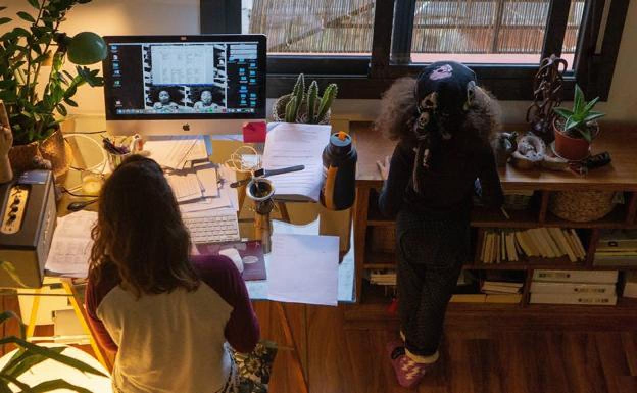 Una mujer realiza teletrabajo en su casa mientras su hija juega a su lado.