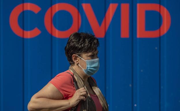 Una mujer pasea ante un cartel de covid. 