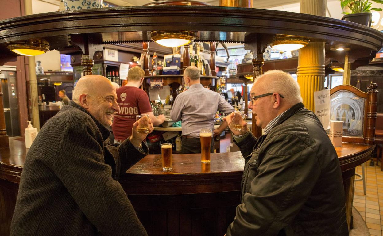 Dos personas toman una cerveza en un bar. 