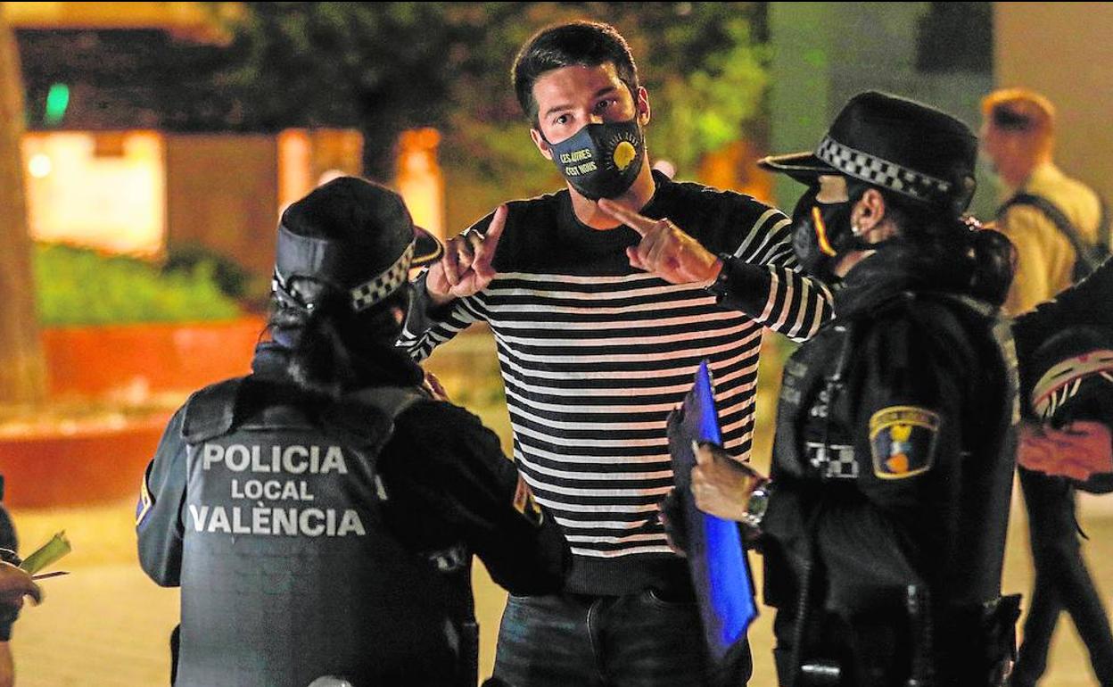 Dos agentes de la Policía Local identifican a los jóvenes que bebían en la vía pública y sin llevar la mascarilla, en la madrugada del viernes en Valencia.