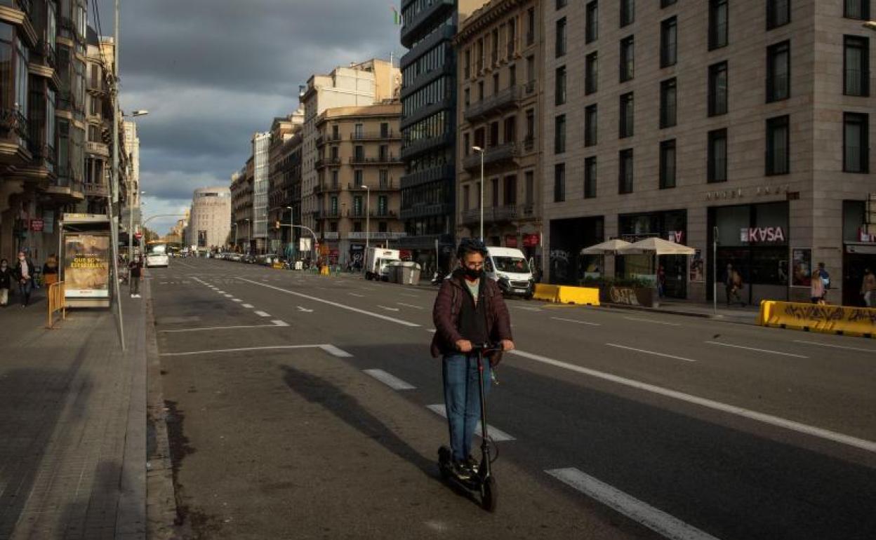 Un joven con mascarilla circula en patinete por Barcelona.