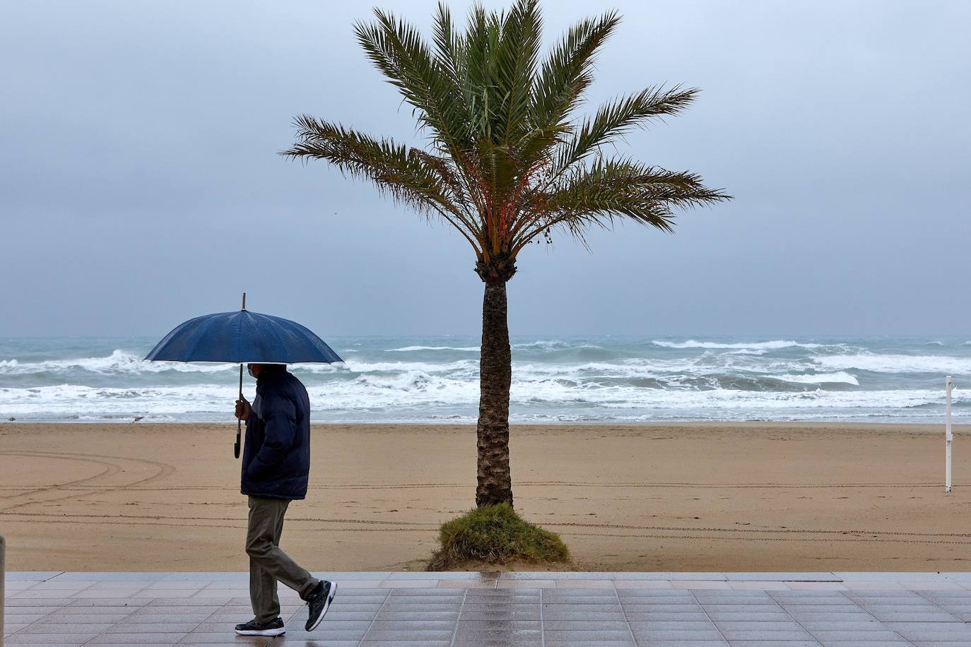 Una persona se protege de la lluvia en el paseo marítimo de Gandía