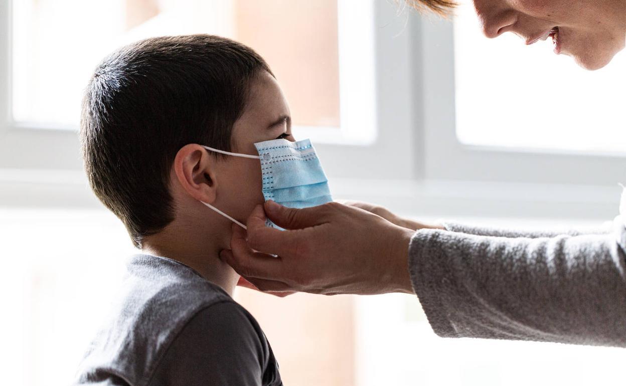 Una madre coloca a su hijo una mascarilla.