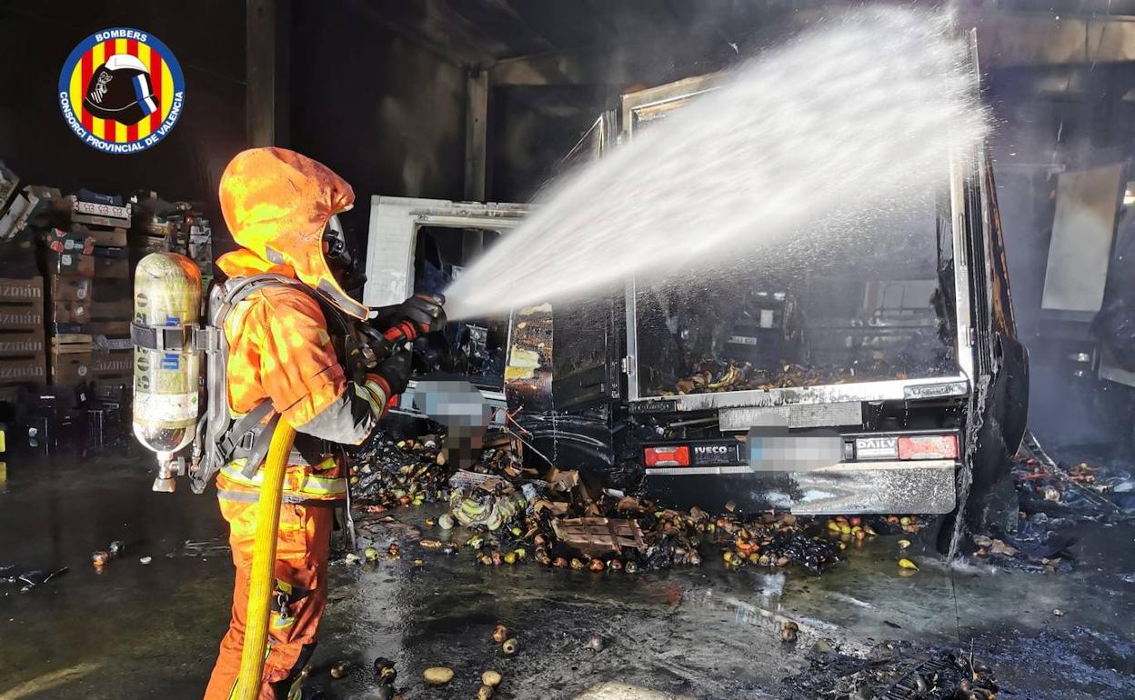 Un bombero lanza agua a uno de los vehículos afectados. 