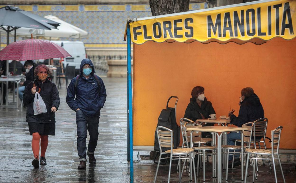 Dos personas en la terraza de un bar protegidas de la lluvia por un toldo de un puesto de flores.