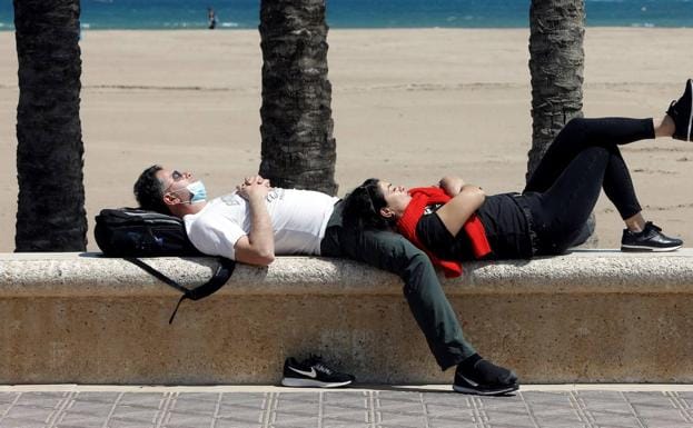 Dos personas descansan al sol en la Malvarrosa de Valencia.. 