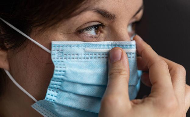 Una mujer se ajusta la mascarilla. 