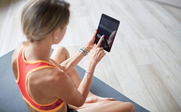 Una mujer consulta una tablet mientras hace ejercicio.