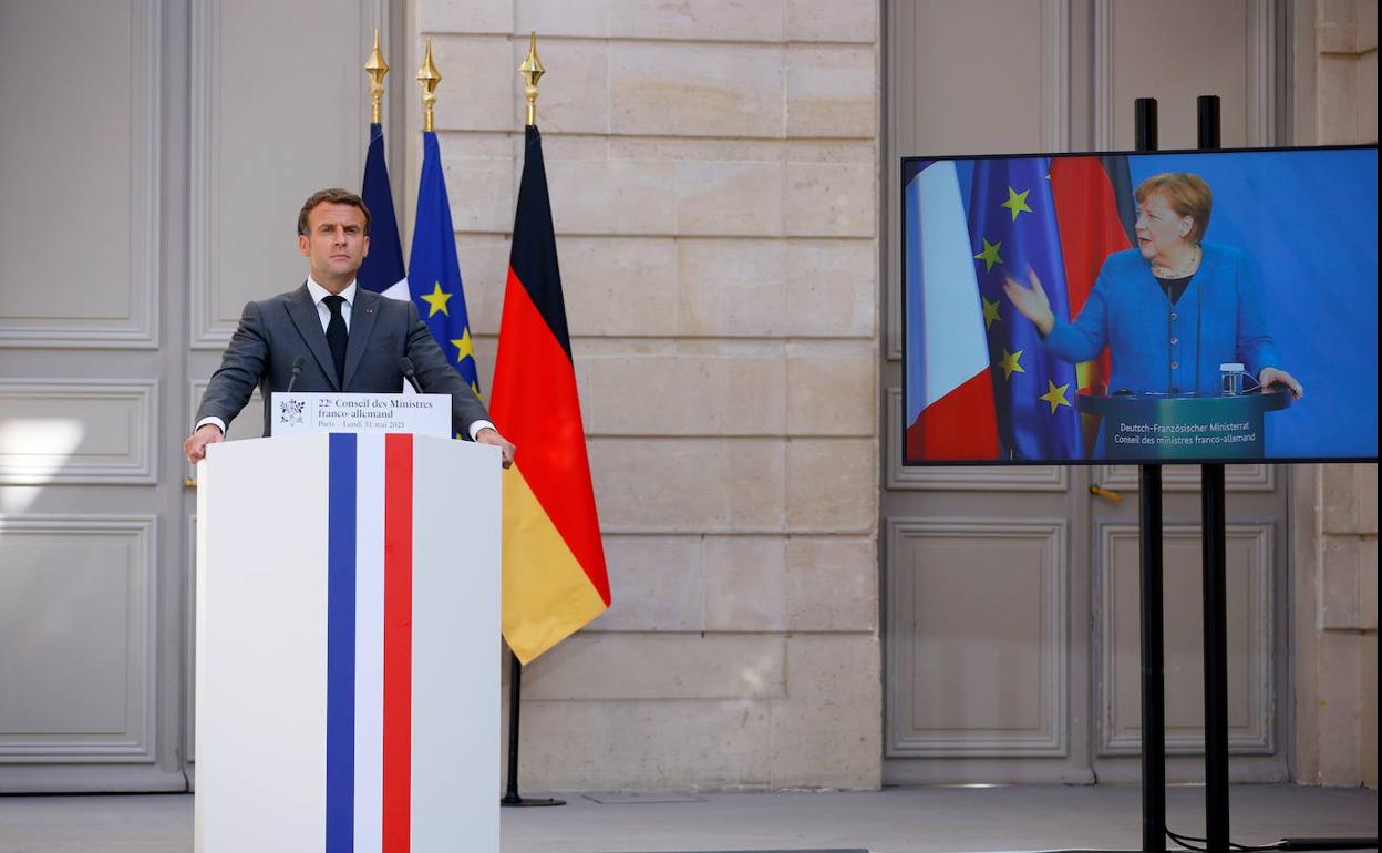 El presidente francés, Emmanuel Macron, y la canciller alemana, Angela Merkel, en la pantalla, se dirigen este lunes a la prensa.