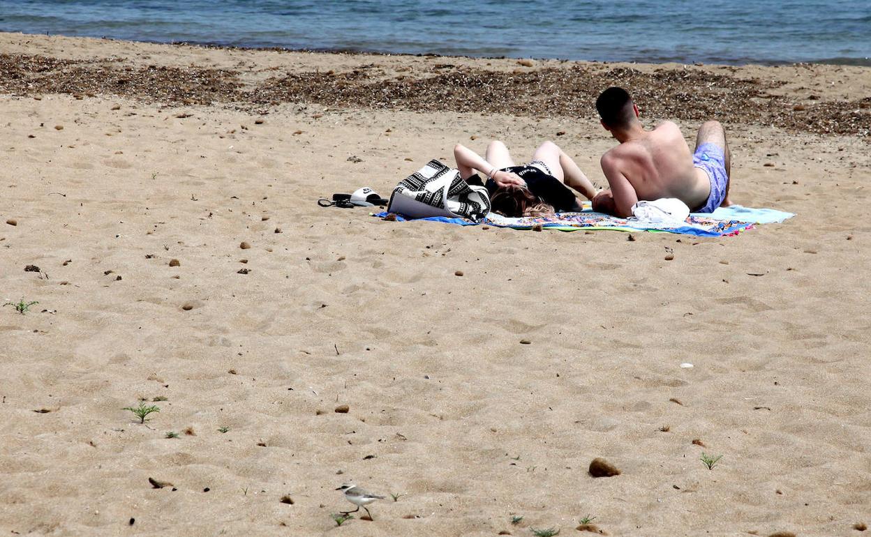 Dos personas tomando el sol en una playa de Dénia. 