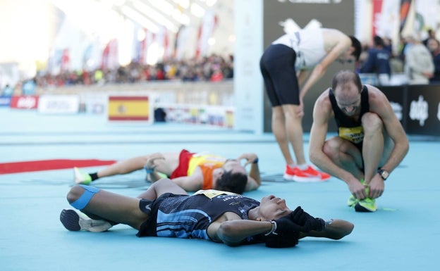 Corredor se ata los cordones junto a dos participantes desolados al finalizar la 10K Valencia 