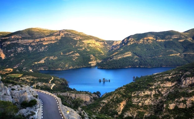 Imagen principal - Arriba, vista aérea del pantano de Bueso. Abajo a la izquierda, el pantano desde la orilla. A la derecha, bañistas observan el islote del pantano. 