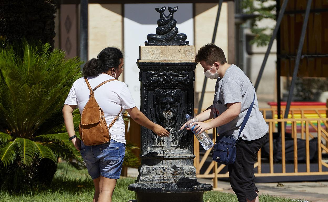 Un pareja llenando una botella de agua en una fuente. 