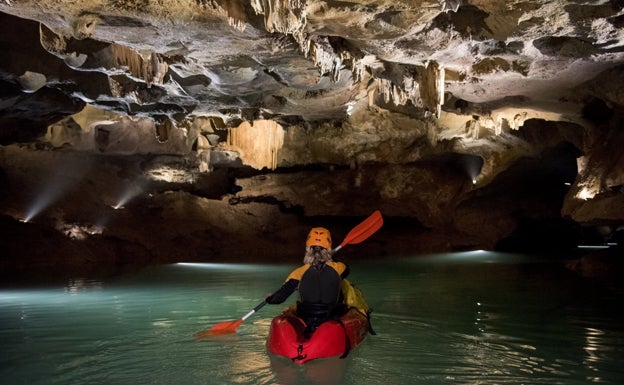 Imagen principal - Arriba, una kayakista recorre las galerías de las cuevas. Abajo a la izquierda, un barquero guía a un grupo por las grutas. Abajo a la derecha, un kayakista observa el techo de las cuevas. 