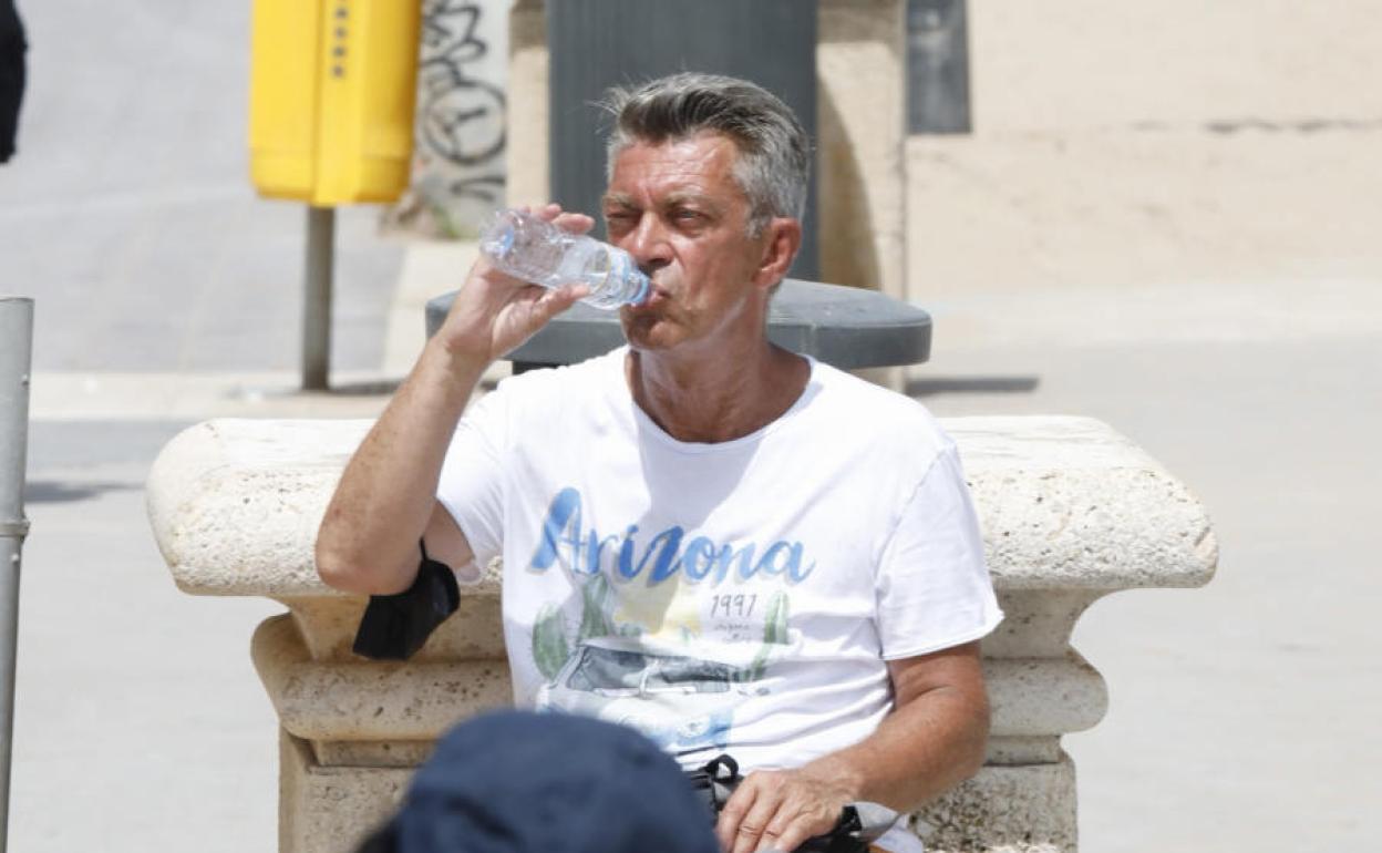 Un hombre bebe una botella de agua en la playa de Valencia.